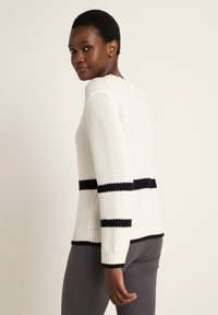 Leichter gestrickter Pullover in Weiß mit schwarzen horizontalen Streifen. Mit rundem Ausschnitt sowie gerippten Bündchen und Saum. Strukturmuster.