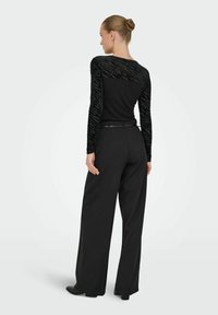 Czarna bluzka z długimi rękawami i teksturowanymi rękawami z siateczki, w połączeniu z szerokimi czarnymi spodniami. Całość dopełnia czarny pasek.