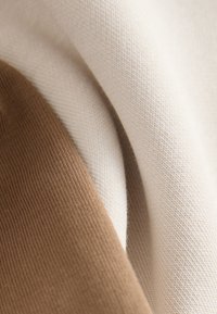 Primo piano di tessuto beige e marrone piegato con trama evidente e luce soffusa che mette in risalto i dettagli del materiale.