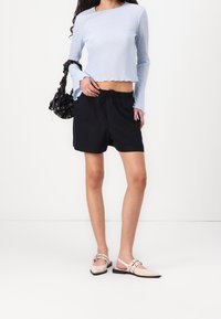 Jasnoniebieski prążkowany top z długim rękawem, czarne szorty z troczkiem oraz beżowe lakierowane buty wsuwane z metalowymi ozdobami. Czarna torebka z wzorem.