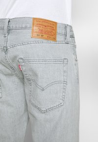 Poche arrière d'un jean Levi's gris clair avec une étiquette rouge Levi's et un label en cuir beige affichant la marque et les détails de la taille.