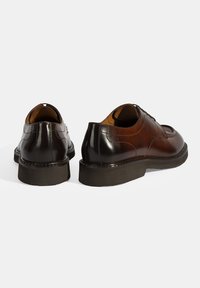 Bruine en zwarte leren nette schoenen met gladde texturen, ronde neuzen en contrasterende donkere rubberen zolen; veters en gestikte details zichtbaar.