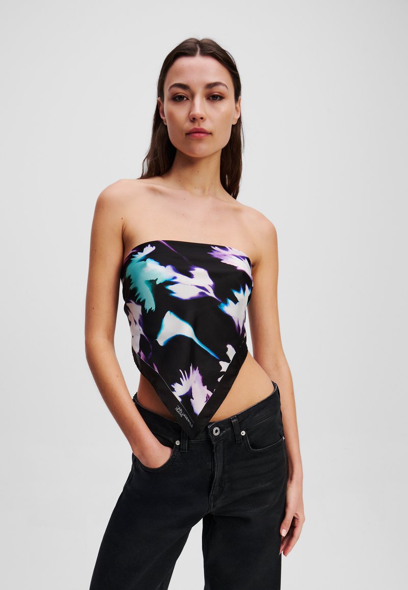 Grafisches schwarzes Bandeau-Top mit floralen Mustern in Lila und Türkis, mit einem dreieckigen Schnitt und kombiniert mit hoch taillierten schwarzen Jeans.