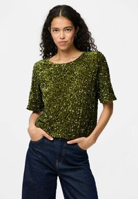 Top verde con paillettes, dal collo rotondo e maniche corte, con una superficie testurizzata e abbinato a jeans in denim scuro.