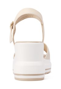 Sandal beige con suola piatta bianca, cinturino testurizzato e fibbia regolabile alla caviglia. Materiale liscio con design minimalista.