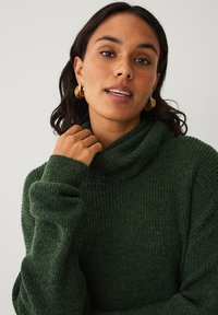 Mørkegrøn, tekstureret turtleneck sweater med ribbet design og lange ærmer. Bemærkelsesværdige detaljer inkluderer en afslappet pasform og en hyggelig halslinning.