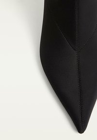 Chaussure noire à bout pointu en tissu lisse. Présente des côtés sans couture et des détails de piqûre. Design léger avec une silhouette épurée.