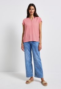 Top rosa de manga corta con escote en forma de pico, combinado con jeans de pierna ancha de color azul claro. La modelo lleva sandalias trenzadas. Ajuste simple y casual.