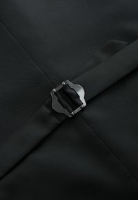 Schwarzer Stoff mit einer strukturierten Oberfläche, versehen mit einem metallischen Schnallendetail in der Mitte. Die Schnalle hat ein markantes geometrisches Design.