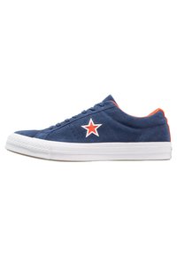 Zapatillas de ante azul marino con acentos naranjas, suela de goma blanca y un logo de estrella roja en el lateral. Presentan una puntera redondeada y un diseño de cordones.