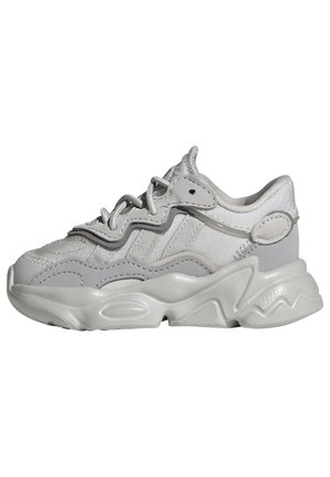 Masywne białe i jasnoszare trampki z falistą podeszwą, teksturowaną cholewką, grubymi sznurowadłami i wyściełanym kołnierzem wokół kostki.