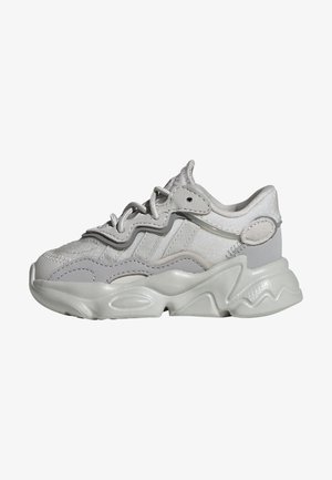 Masywne białe i jasnoszare trampki z falistą podeszwą, teksturowaną cholewką, grubymi sznurowadłami i wyściełanym kołnierzem wokół kostki.