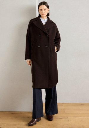 Langer, brauner Wollmantel mit doppelter Knopfleiste, Reverskragen, Seitentaschen und glatter Textur, kombiniert mit navyfarbener Nadelstreifenhose.
