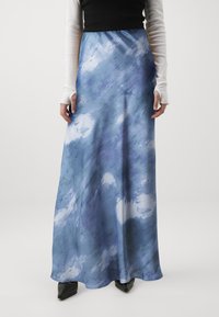 Sinisesti ja valkoisesti raidallinen maksihame, joka on valmistettu valuvasta kankaasta ja jossa on abstrakti pilvimäinen kuvio. Päällä musta toppi ja kärkitossut mustina.