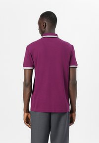 Lila Poloshirt mit kurzen Ärmeln und Kragen, mit kontrastierenden gestreiften Akzenten am Kragen und den Ärmelsäumen. Flache Stofftextur.