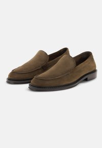 Mocassins marron en daim à enfiler avec semelle noire cousue et petit talon empilé, présentés sur fond blanc.