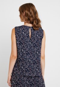 Marinebluse mit ärmellosem Design, ausgestattet mit einem floralen Muster in Pink, Weiß und Blau sowie einem Schlüsselaugen-Detail auf der Rückseite.