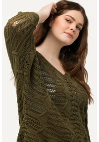 Olivgrüner Strickpullover mit einem strukturierten Muster aus hexagonalen Designs und offenen Maschen. V-Ausschnitt und lange Ärmel.