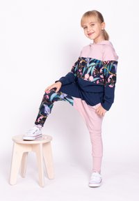 Bluza z kapturem w kolorze granatowym i różowym z kwiatowym wzorem; zestawiona z różowymi i wzorzystymi legginsami; modelka pozuje na jasnym drewnianym stołku.