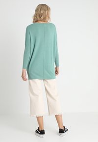 Mintgrön oversized stickad tröja med ribbade ärmar, matchad med off-white korta byxor med fransade fållar och svarta sneakers.