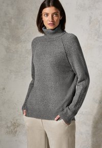 Grauer, gestrickter Rollkragenpullover mit gerippten Bündchen und Saum, in lockerer Passform und mit glatter Textur. Kombiniert mit hellbeigen Hosen.