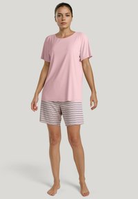 Lichtroze top met korte mouwen, gecombineerd met gestreepte shorts in wit, marineblauw en kastanjebruin. Zacht materiaal, ontspannen pasvorm en shorts tot halverwege de dij.