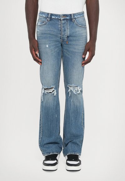 Lichtblauwe verwerkte denim jeans met gescheurde knieën, losse pasvorm en rafelige zomen, gedragen met zwart-witte sneakers.