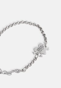 Sølvkjede-armbånd med en hjerteanheng som har et design av dødningehode og kryssebein, gravert tekst og en sikker lås.