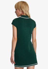 Grünes, geripptes Kleid mit tailliertem Design, kurzen Puffärmeln und weißer Borte am Kragen und Saum, ausgestattet mit einem Logo-Tag auf der Rückseite.