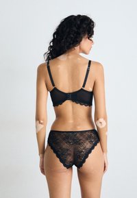 Black lace bra with scalloped edges and adjustable straps, paired with matching lace brief featuring floral patterns, viewed from the back.