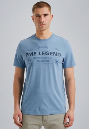T-shirt en coton bleu clair à manches courtes, présentant un texte et des graphiques noirs liés à un design d'avion de transport sur le devant.