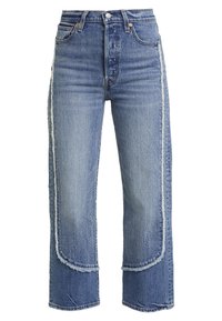 Denimjeans med lys blå vask, højt talje, vide ben, frynset kant og kontrastfulde lapdetaljer med lysere denimstykker på siderne.