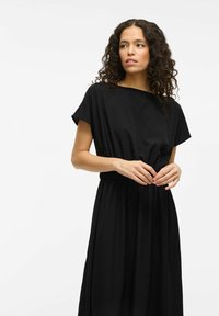 Black dress with short sleeves, elastic waist, and a flowing silhouette. Made of smooth fabric with a minimalist design and no visible patterns.