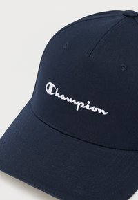 Μπλε σκούρο μπλε καπέλο του μπέιζμπολ με λευκό κεντημένο λογότυπο «Champion» στο μπροστινό μέρος, με ραμμένες τρύπες αερισμού και κυρτό γείσο.