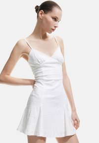 Vestido blanco sin mangas con escote en V, tejido texturizado, cintura fruncida y falda acampanada. Presenta delicados bordados y finas correas ajustables.