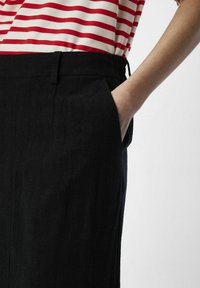 Un pantalon noir à finition texturée, doté de poches latérales et d'une taille élastique, associé à un haut rayé rouge et blanc.