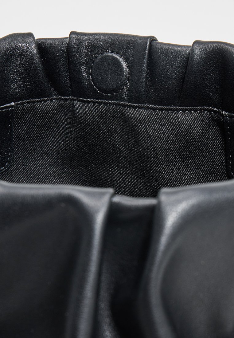 Bolso de mano de cuero negro con parte superior fruncida, que cuenta con un cierre a presión y una textura suave. El interior está forrado con tela negra.