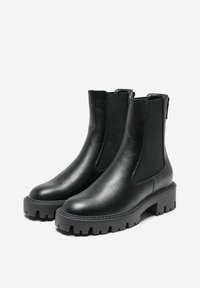 Botas de cuero negro hasta el tobillo con paneles laterales elásticos, suela gruesa y diseño de banda de rodadura resistente para tracción. Textura suave y detalles mínimos.