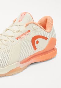 Sport shoes with a cream and coral color scheme. Textured mesh upper, reinforced toe, and a cushioned sole with an orange accent detail.
