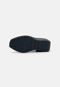Semelle de chaussure en caoutchouc noir avec un motif de semelle géométrique, présentant une surface texturée et un marquage. Le design est robuste et plat.