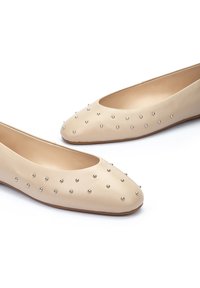 Bailarinas de cuero beige con puntera redondeada, que cuentan con tachuelas de metal distribuidas uniformemente por la parte superior y un forro interior suave.