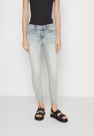 Jeans ajustados de color azul claro con un ligero desvanecimiento y un diseño clásico de cinco bolsillos, combinados con sandalias negras con hebillas y acentos de tachuelas.