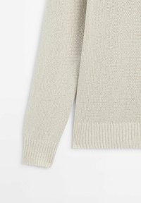 Pullover in maglia beige chiaro con una trama allentata, polsini e orlo a coste. Il tessuto è strutturato, offrendo un aspetto accogliente.