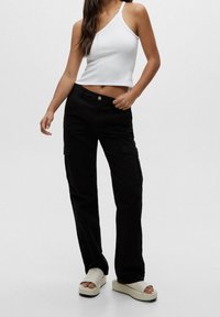 Biała prążkowana, bezrękawnikowa crop top z jednym ramiączkiem, w połączeniu z luźnymi czarnymi spodniami cargo. Całość dopełniają masywne beżowe sandały na platformie.