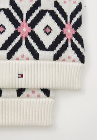 Un tricot à motifs avec une base crème et des designs géométriques en marine, noir et rose. Les poignets côtelés ajoutent de la texture et du contraste.