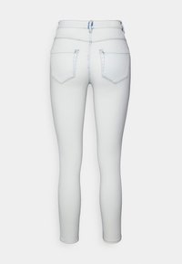 Jeans skinny brancos feitos de denim, com uma cintura alta, dois bolsos traseiros, costura em azul claro e uma textura suave.