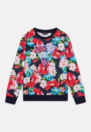 Sweat-shirt bleu marine avec motif floral rose, rouge et bleu, arborant un grand triangle bleu avec le logo "GUESS" et un point d'interrogation sur le devant.