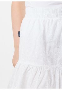 Hvid bomuldsnederdel med broderet blomsterdesign, sammenpresset talje for en god pasform, og flæset kant. Har et side-label mærket "SEASIDE."