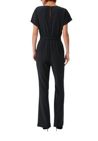 Czarny kombinezon z dopasowanym wcięciem w talii, krótkimi rękawami i wycięciem w kształcie okna z tyłu. Rozszerzane nogawki oraz gładka faktura podkreślają jego sylwetkę.