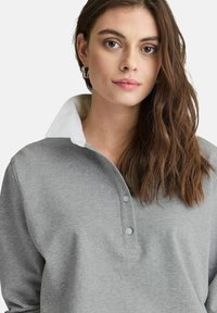 Grå sweatshirt med vit krage, med knappslå och mjuk textur. Långa ärmar och avslappnad passform.